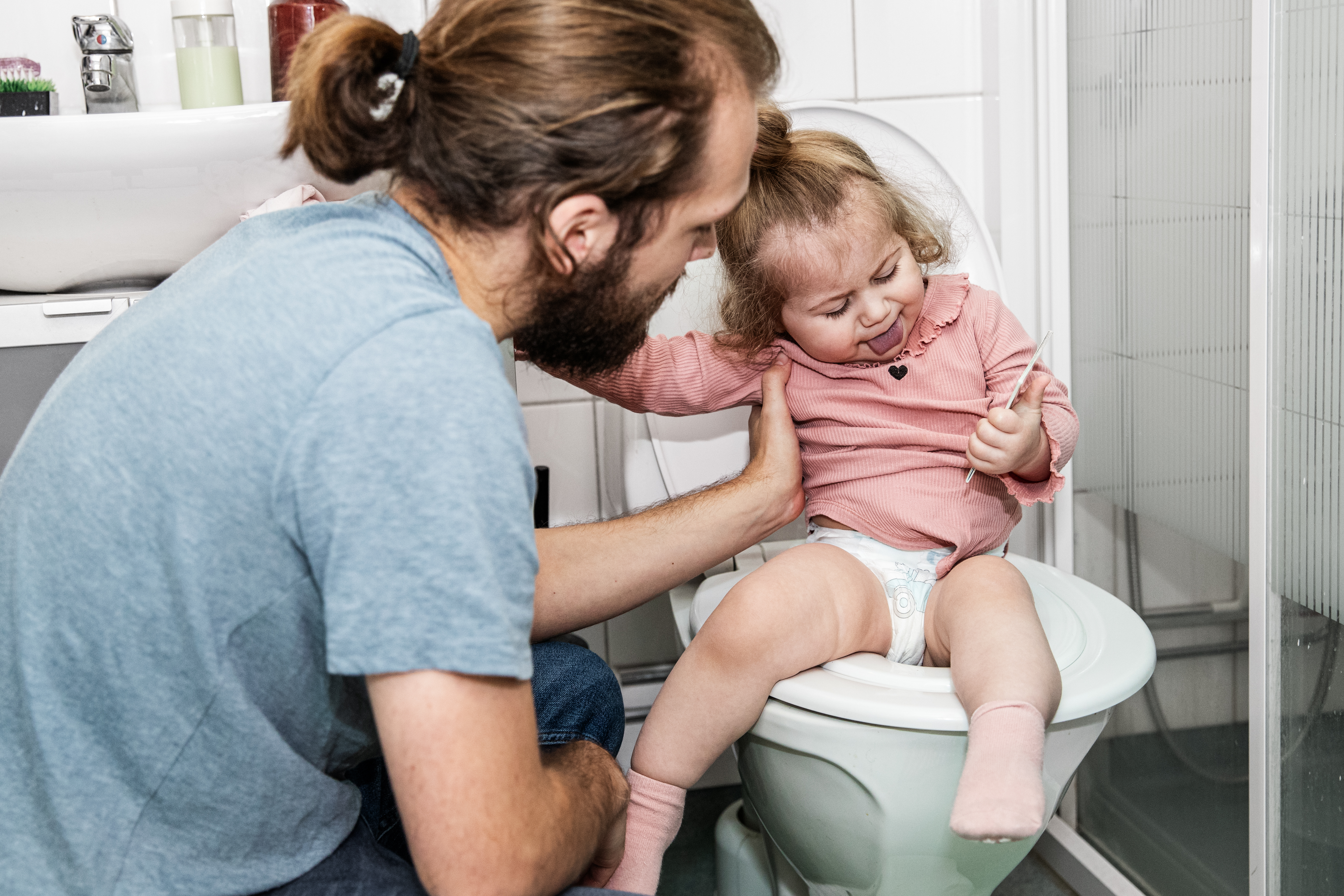 Förälder och ett barn som sitter på toaletten med blöja på.