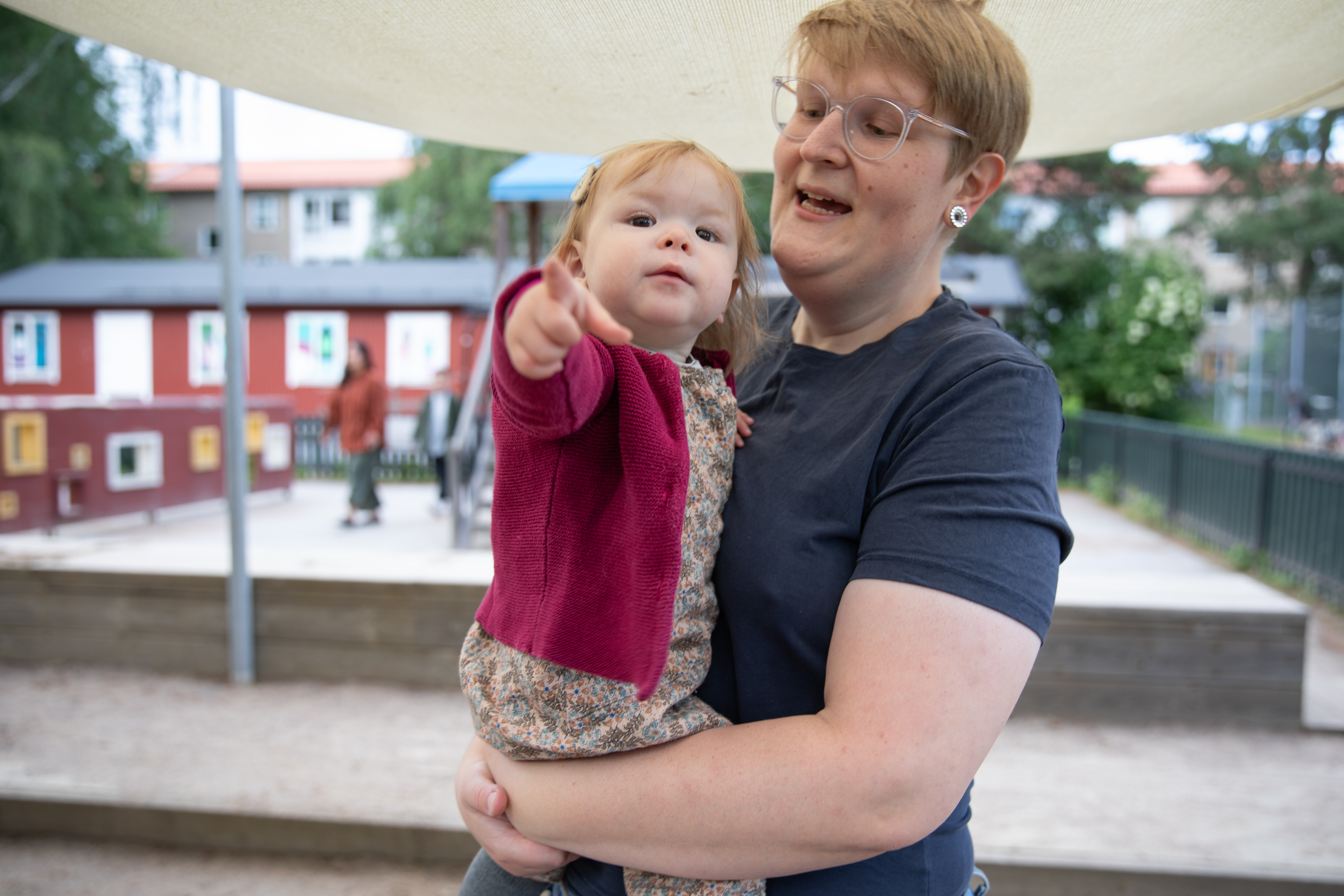 barnet sitter i förälderns famn och pekar mot den som fotograferar 