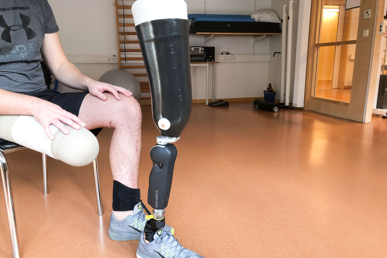 En person sitter på en stol och har en benprotes stående framför sig.