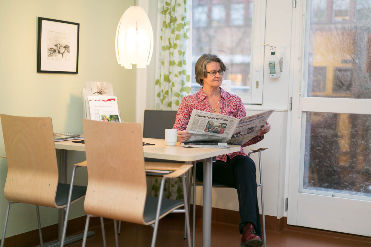 Person sitter vid ett bord och läser en tidning.
