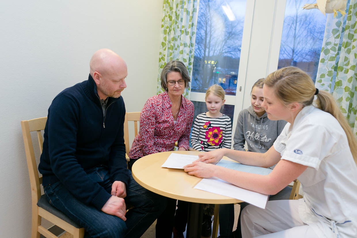 En familj sitter runt ett bord tillsammans med en vårdperson som visar något på ett papper.