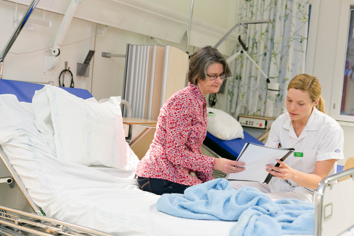 En patient och en vårdperson tittar på ett dokument tillsammans i ett vårdrum.