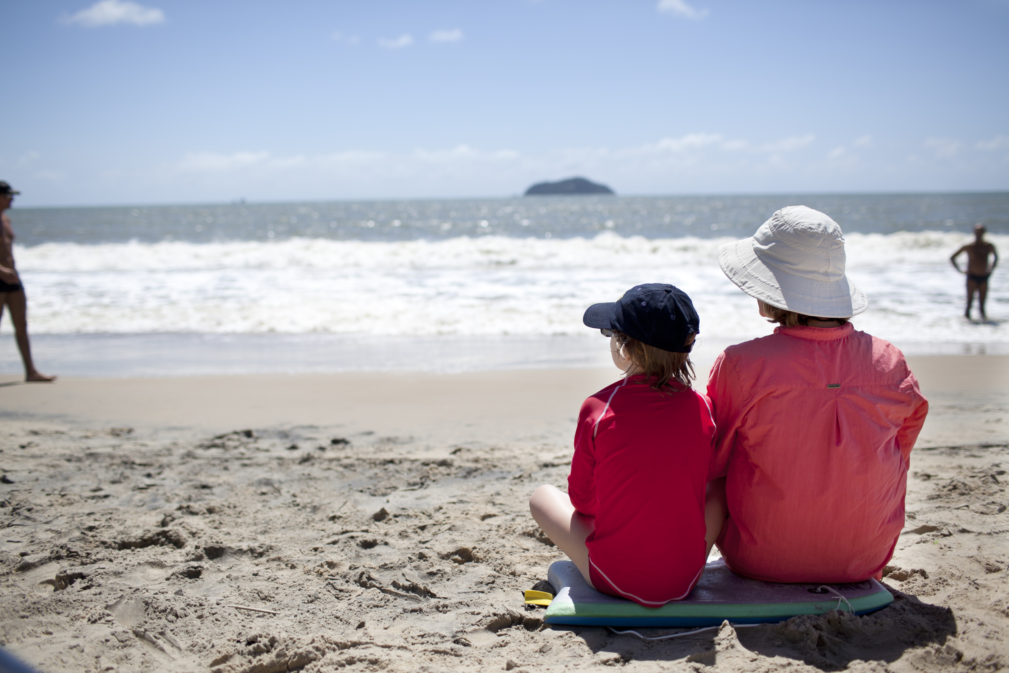Två personer som sitter på stranden med keps och solhatt.